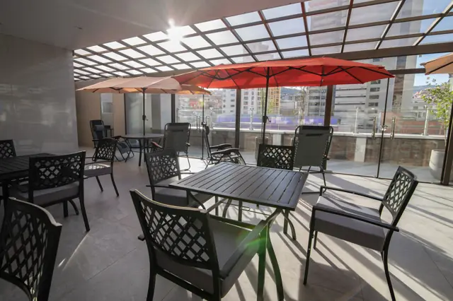 Terraza techada con mesas, sillones y sombrillas rojas